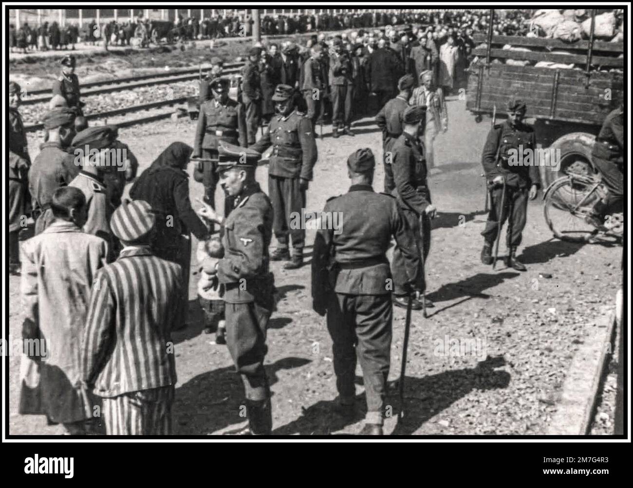 AUSCHWITZ-BIRKENAU, PRIGIONIERI IN FILA PER L'ARRIVO IN CODA, Una visione dell'inferno sulla terra. 1944, i nazisti "giudicano" (vita o morte) ignari prigionieri in convoglio ferroviario fuori dall'ingresso del campo di sterminio di Auschwitz-Birkenau. Il famigerato campo di Auschwitz fu iniziato per ordine di Adolf Hitler nel 1940 durante l'occupazione della Polonia da parte della Germania nazista durante la seconda guerra mondiale, ulteriormente reso possibile da Heinrich Luitpold Himmler il Reichsführer dello Schutzstaffel, e membro leader del Partito nazista di Germania Foto Stock