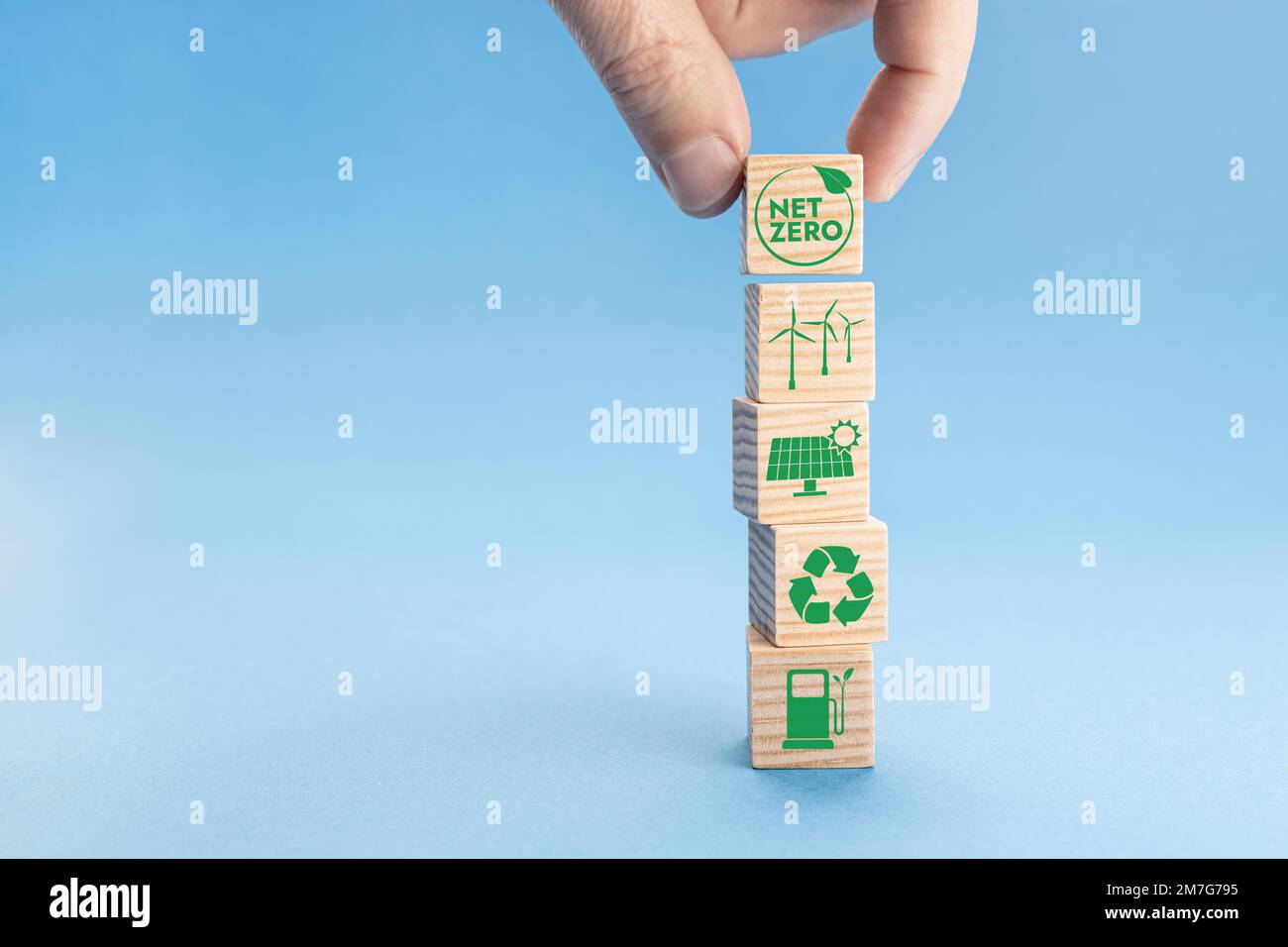 Concetto di zero netto e neutro rispetto al carbonio. Mano che mette il blocco di legno con l'icona di zero netto sulla parte superiore di altri con le icone verdi di energia. Sfondo blu. Spazio di copia Foto Stock