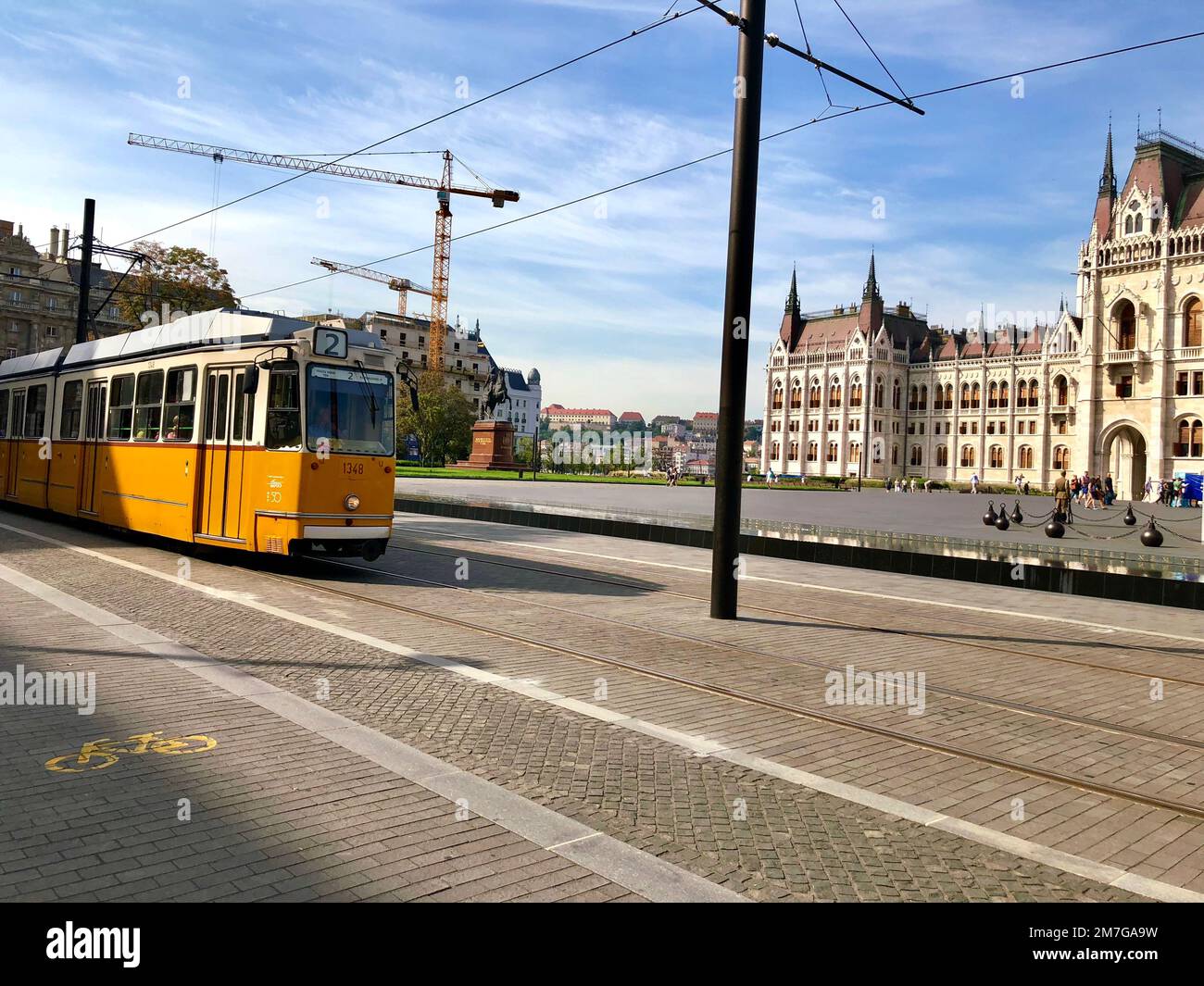 Budapest/Ungheria - 23 settembre 2019: Un tram giallo che passa davanti al Parlamento. Gru gialle sullo sfondo Foto Stock