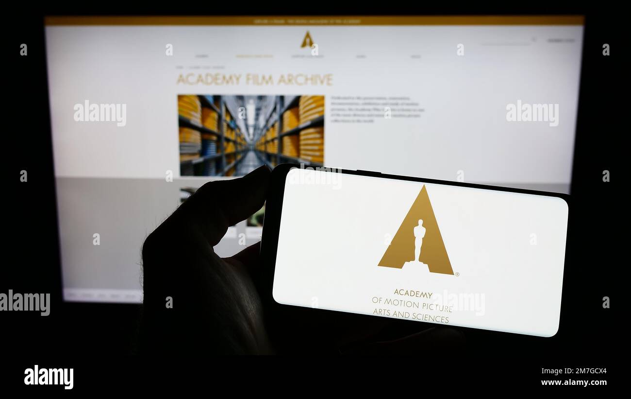 Persona che tiene il cellulare con il logo di Academy of Motion Picture Arts and Sciences (AMPAS) sullo schermo di fronte alla pagina web. Messa a fuoco sul display del telefono. Foto Stock