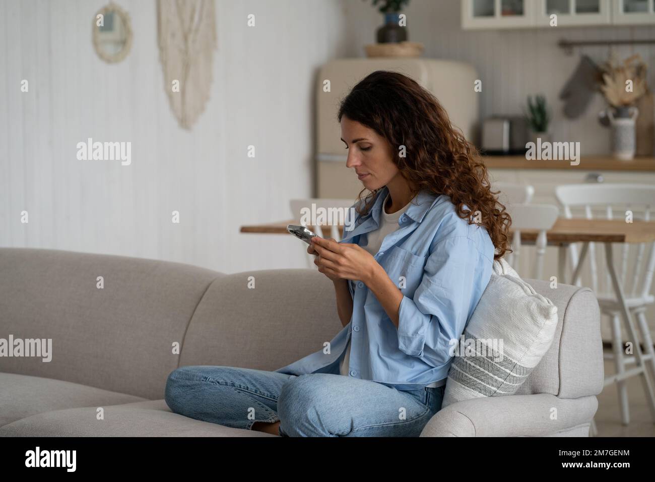 Donna introversa concentrata con smartphone sedersi sul divano con le gambe sotto nel soggiorno Foto Stock