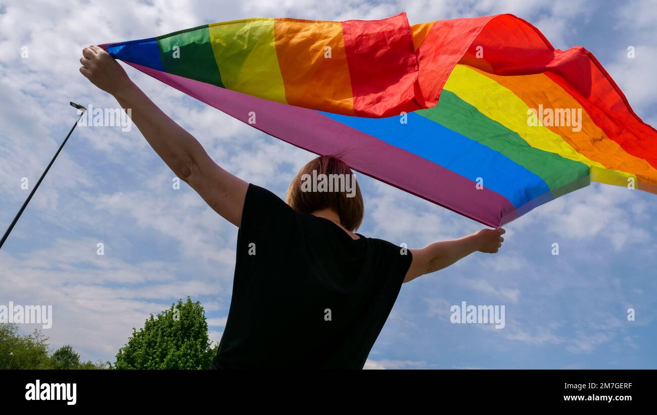 LGBTQIA mese orgoglio, arcobaleno bandiera di pace contro il cielo blu con le nuvole in una giornata di sole. Tenere la donna in mano e celebrare la bisessualità Day o National Coming out Day Foto Stock