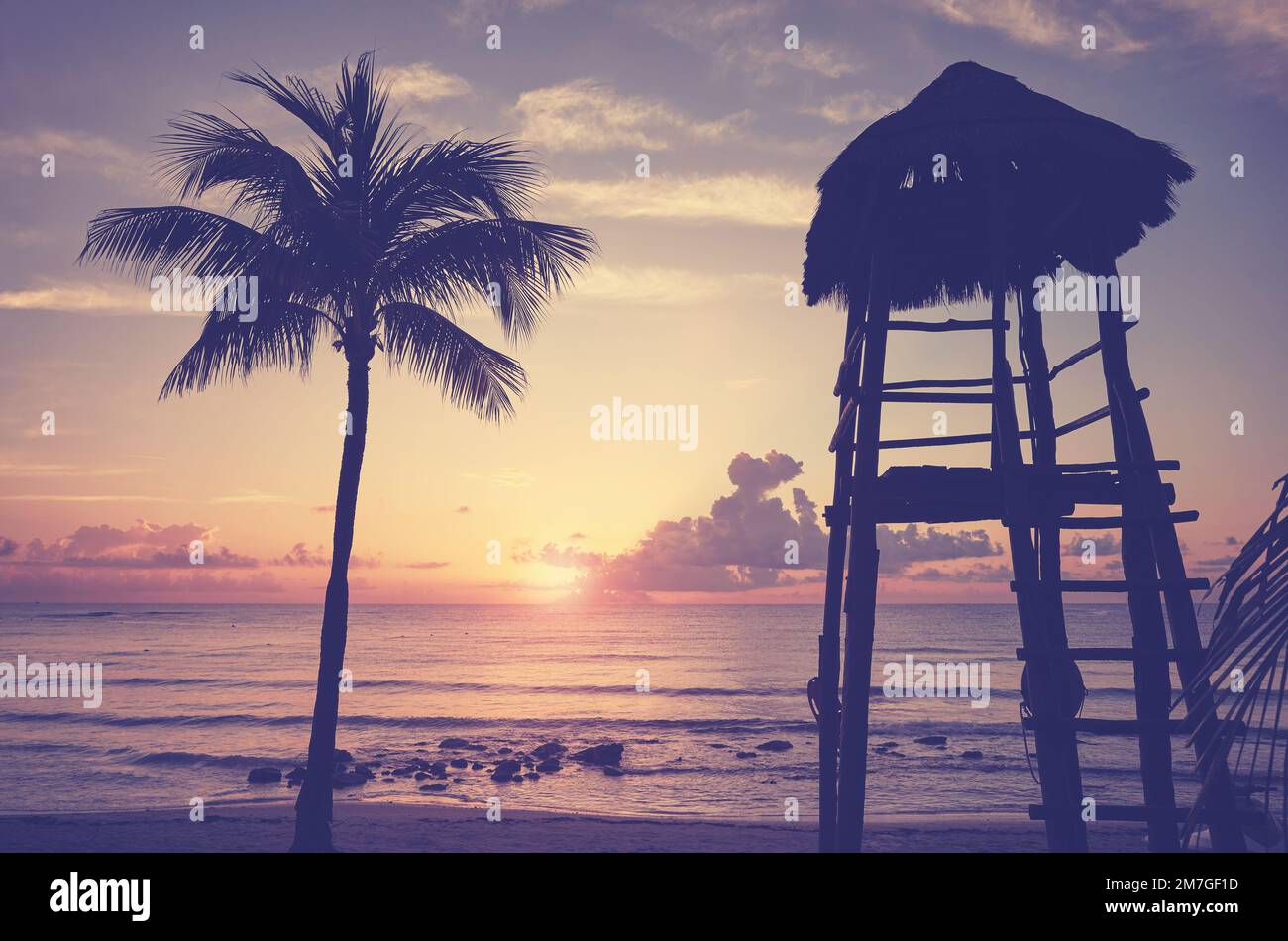 Spiaggia tropicale con silhouette di palme da cocco e bagnino torre al tramonto, tonalità di colore applicato. Foto Stock