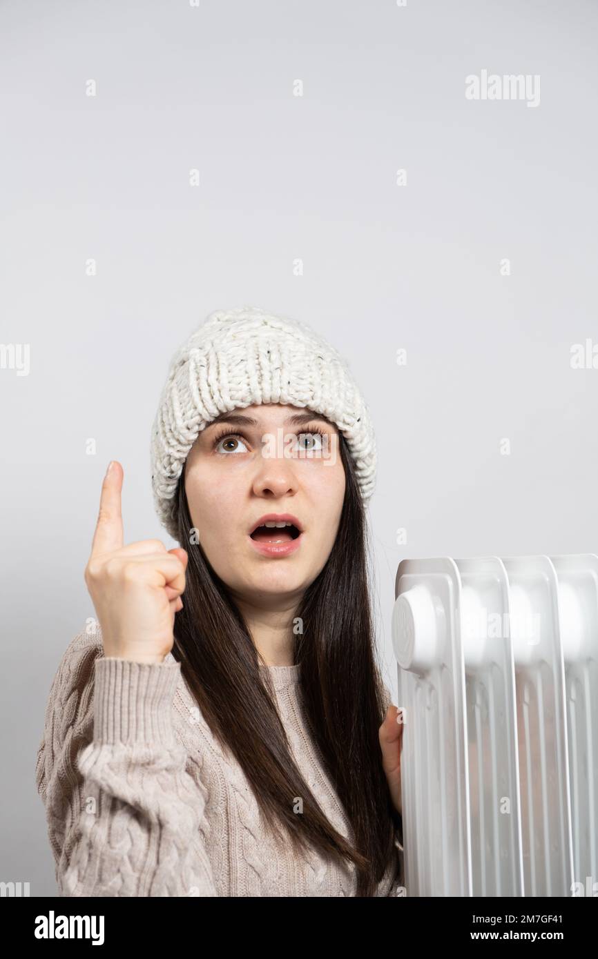 Una donna in un cappello che si scalda vicino al riscaldatore dell'olio e guarda e punta con il dito Foto Stock