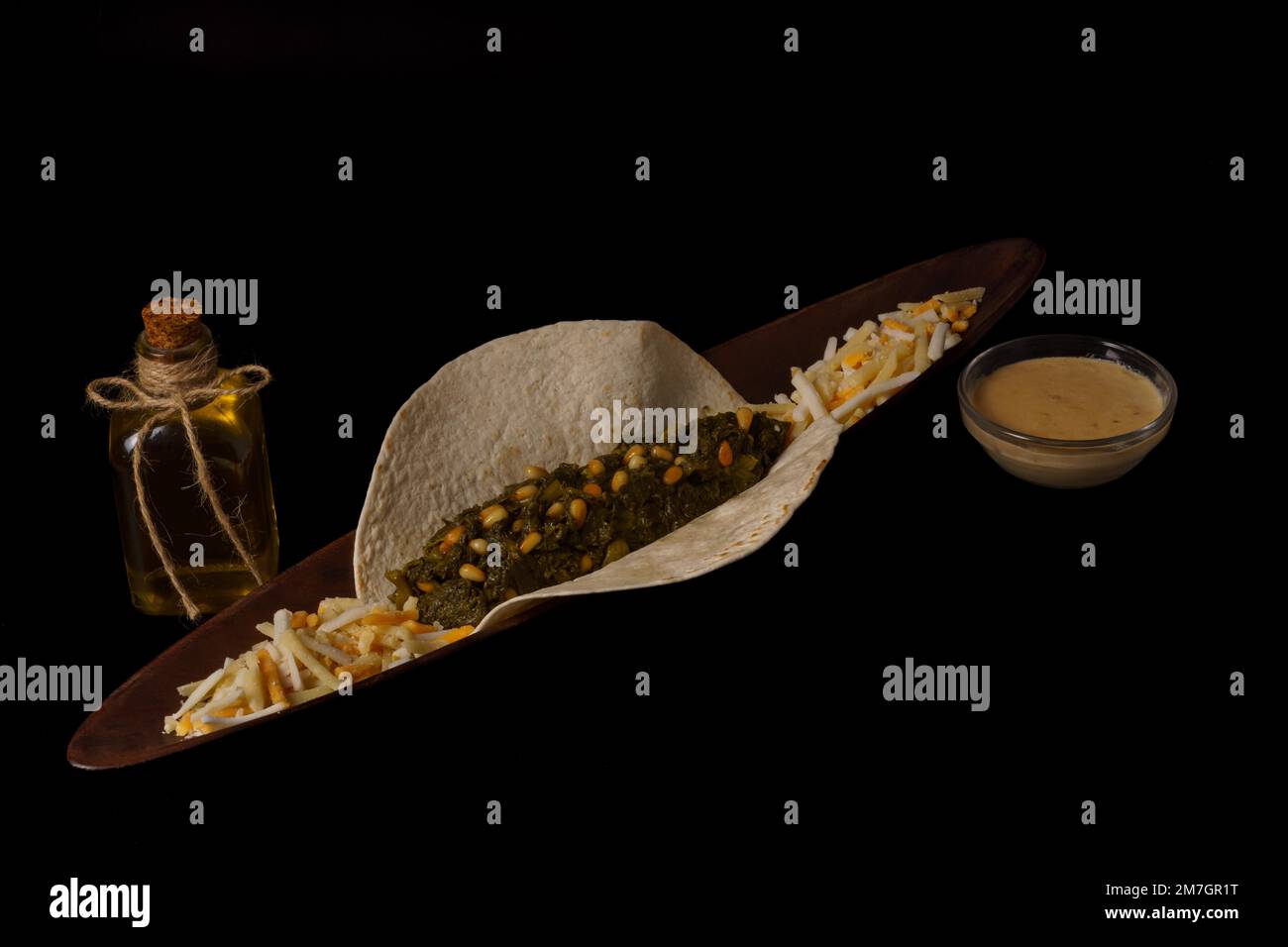 Taco con ciotola di spinaci e pinoli con salsa di formaggio e diversi tipi di formaggio come guarnire bottiglia di olio d'oliva e fondo nero Foto Stock