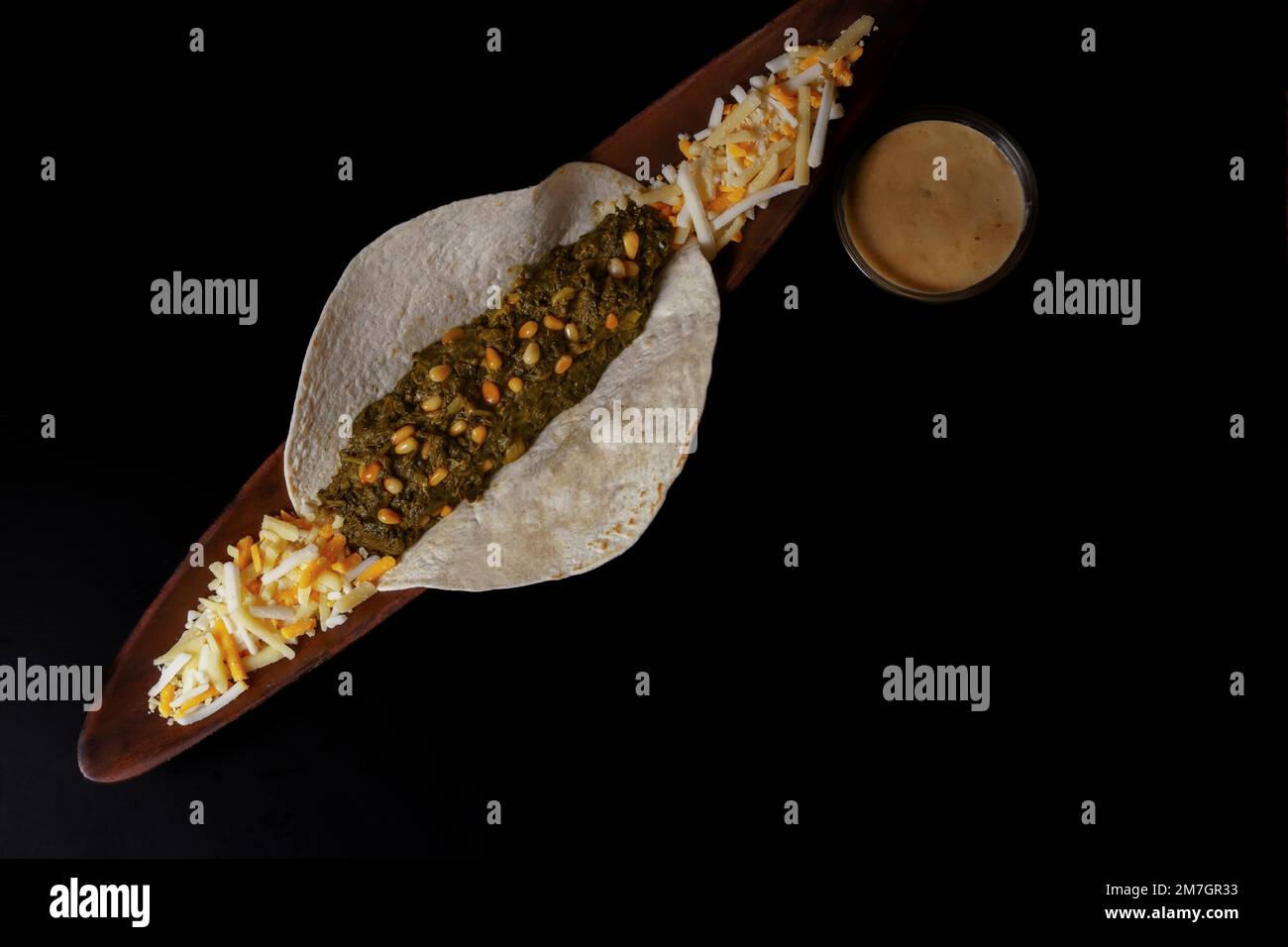 Taco con ciotola di spinaci e pinoli con salsa di formaggio e vari tipi di formaggi come guarnitura e fondo nero Foto Stock