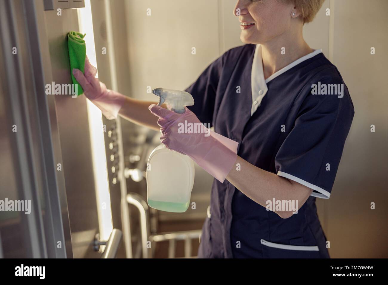 Primo piano della cameriera che indossa uniforme e guanti pulizia ascensore con detergente e straccio Foto Stock
