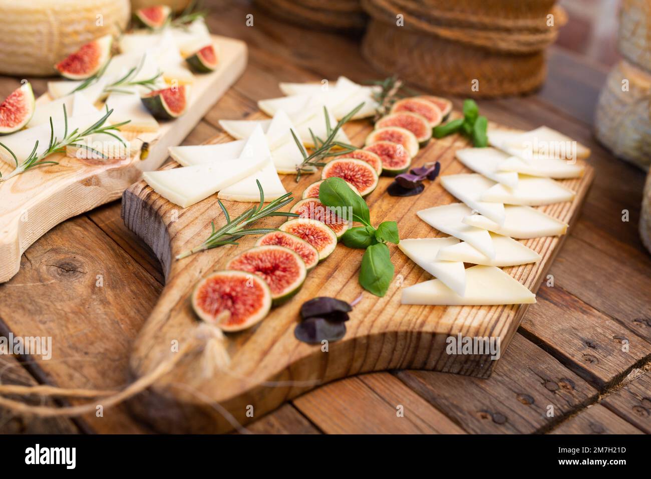 Fette di delizioso formaggio da degustazione, servite con fichi e rosmarino su un tavolo di legno in cantina Foto Stock