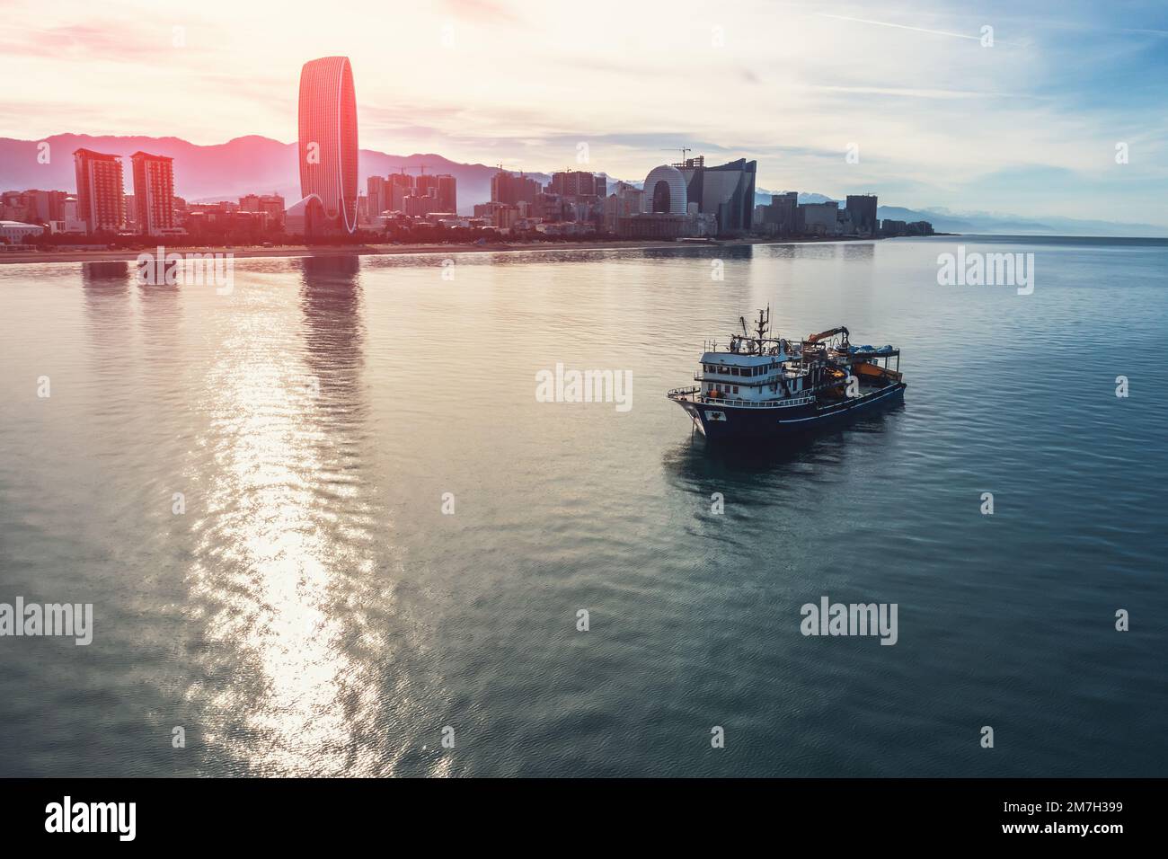 Imbarcazione da pesca sulla superficie del mare vicino alla costa della città con edifici, vista aerea dal drone. Industria della pesca e dei frutti di mare. Foto Stock