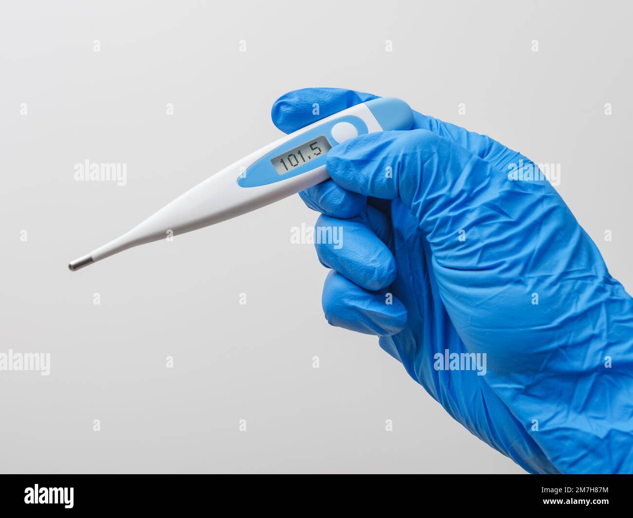 Mano in guanto blu con termometro digitale su sfondo bianco. Operatore medico che indossa guanti protettivi per il controllo del termometro medico. Foto Stock