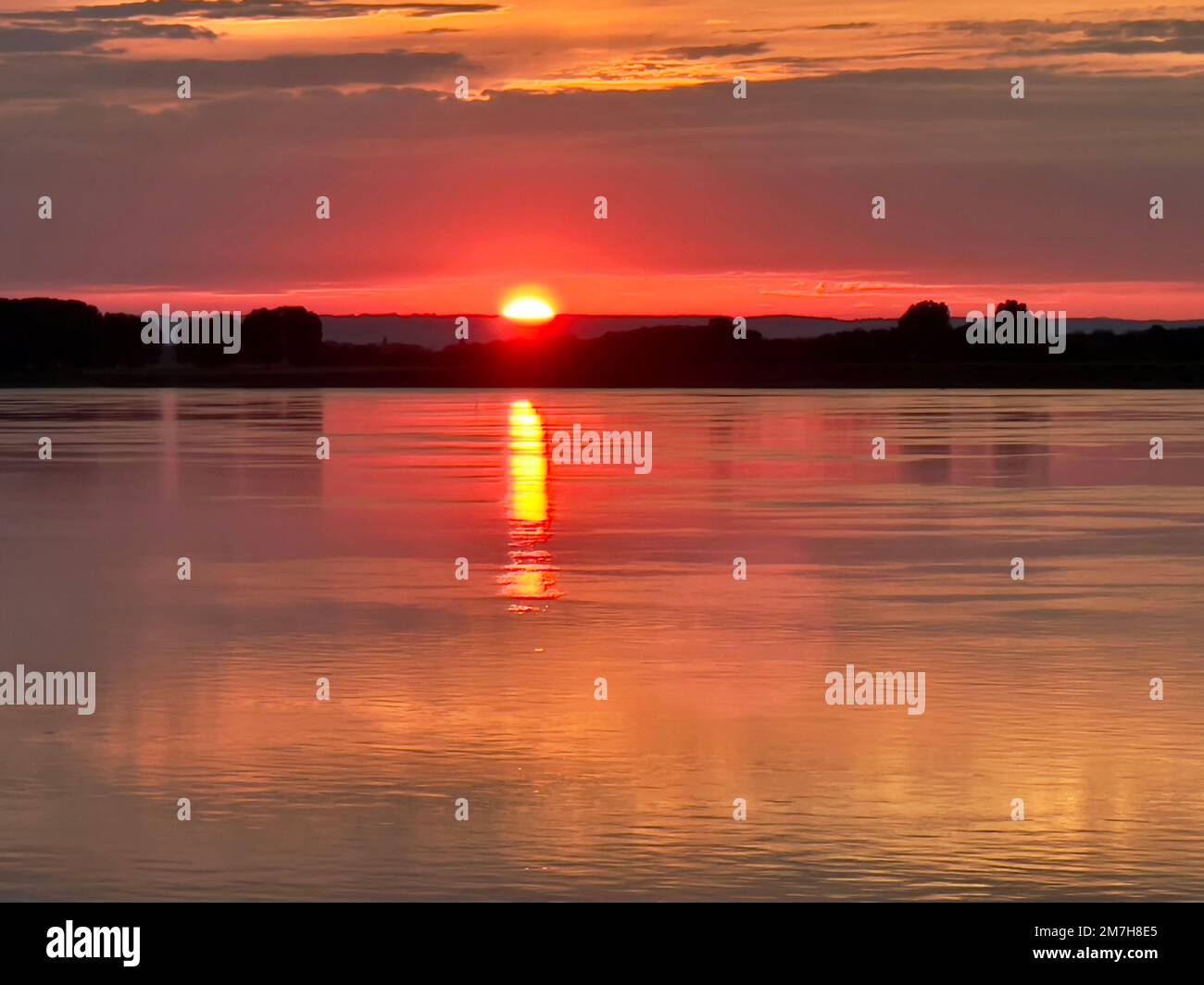Ammira il tramonto sul Danubio da un battello fluviale in Bulgaria. Il riflesso delle striature di sole attraverso le acque calme. Le colline sullo sfondo sono in ombra. Foto Stock