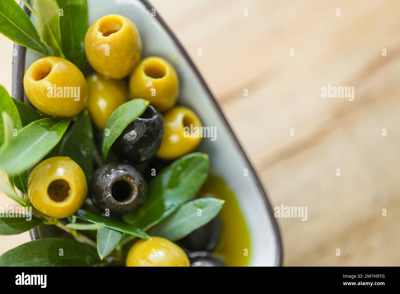 Olive e olio d'oliva. Ingrediente della cucina mediterranea. Olive nere e verdi e un ramo di olive verdi da vicino su un tavolo di legno. Fresco biologico Foto Stock