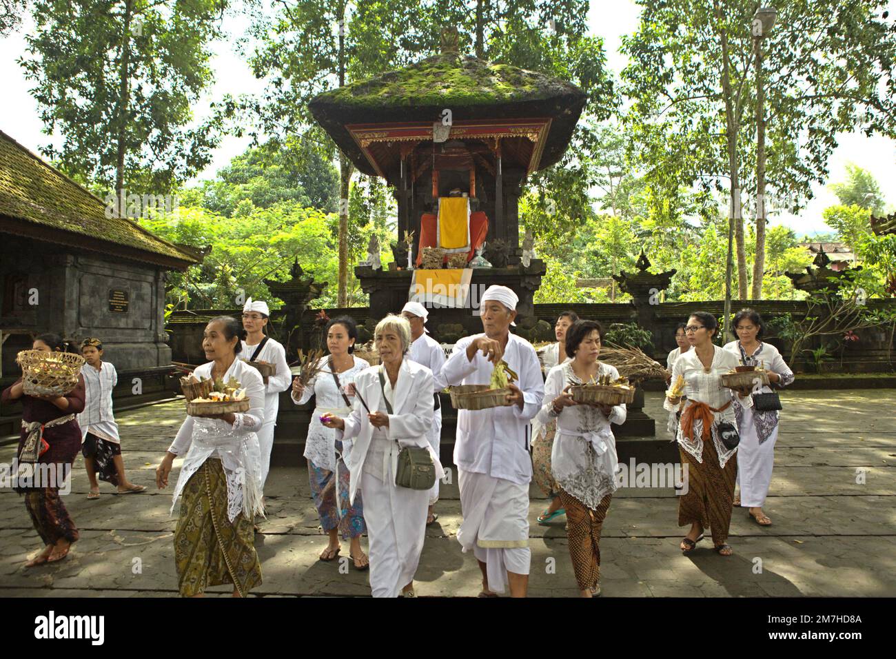 Un prete balinese sta in piedi davanti alle donne di un clan che stanno portando offerte spirituali durante una processione per onorare e purificare gli spiriti dei loro ultimi membri della famiglia, in un tempio situato nel complesso del tempio di Besakih, sul pendio del Monte Agung a Karangasem, Bali, Indonesia. Foto Stock