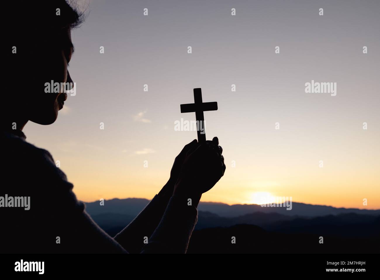 Silhouette di donna cristiana che prega a mano, donna che tiene un crocifisso che prega, spiritualità e religione, donna che prega a dio. Concetto di Cristianesimo. Foto Stock