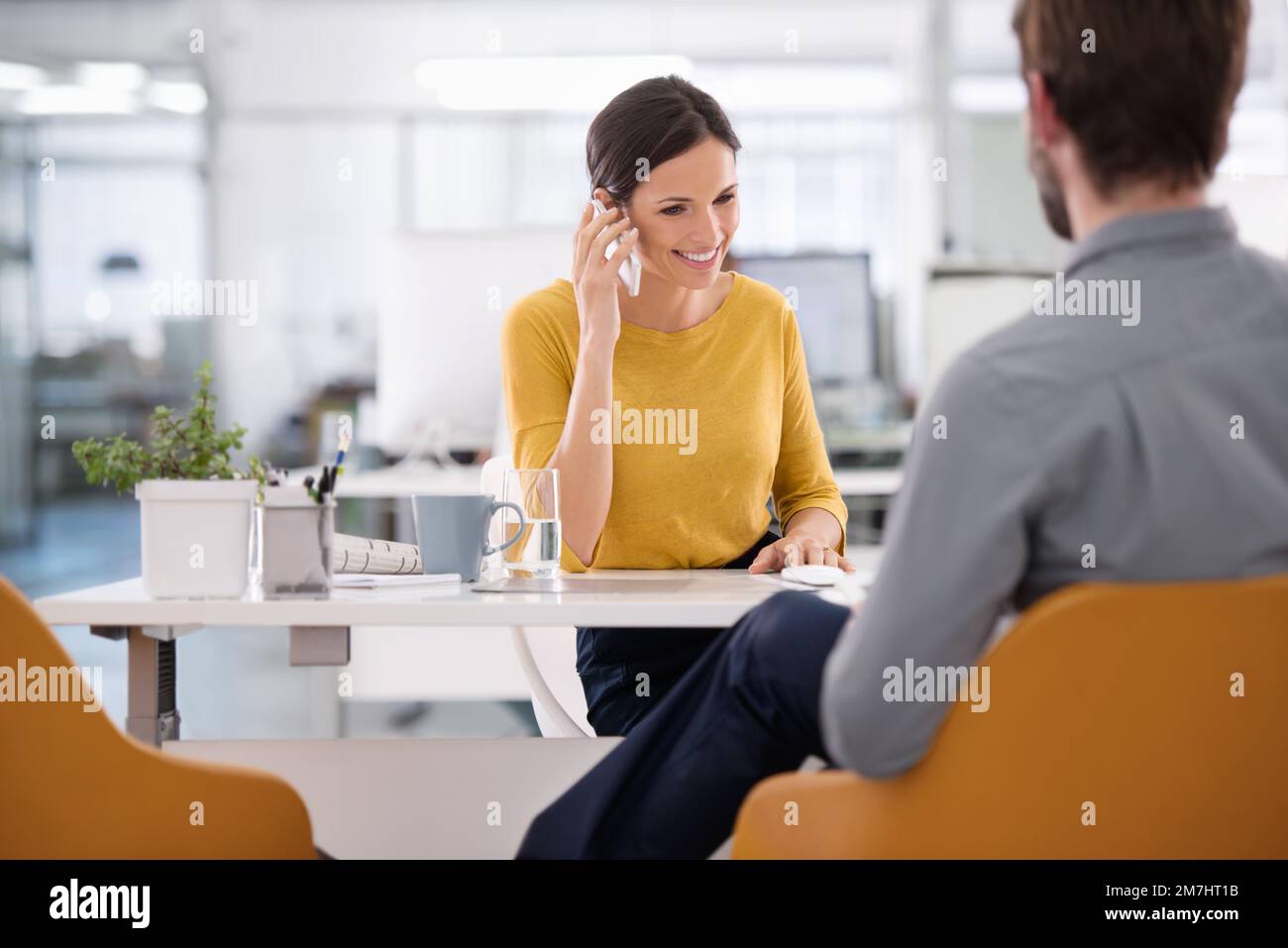 Così dici youre a bordo. una donna d'affari seduta con una collega a un tavolo che parla sul suo telefono cellulare. Foto Stock