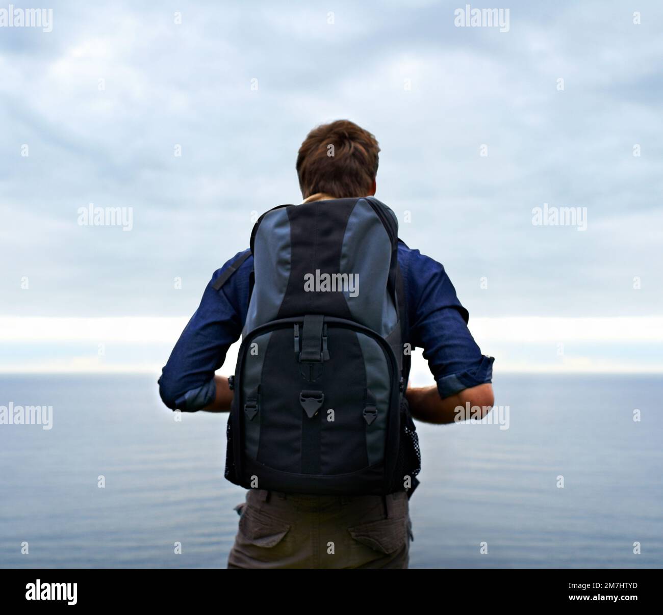 La vita di un avventuriero...Vista posteriore di un giovane uomo in piedi e che guarda fuori su una distesa d'acqua. Foto Stock