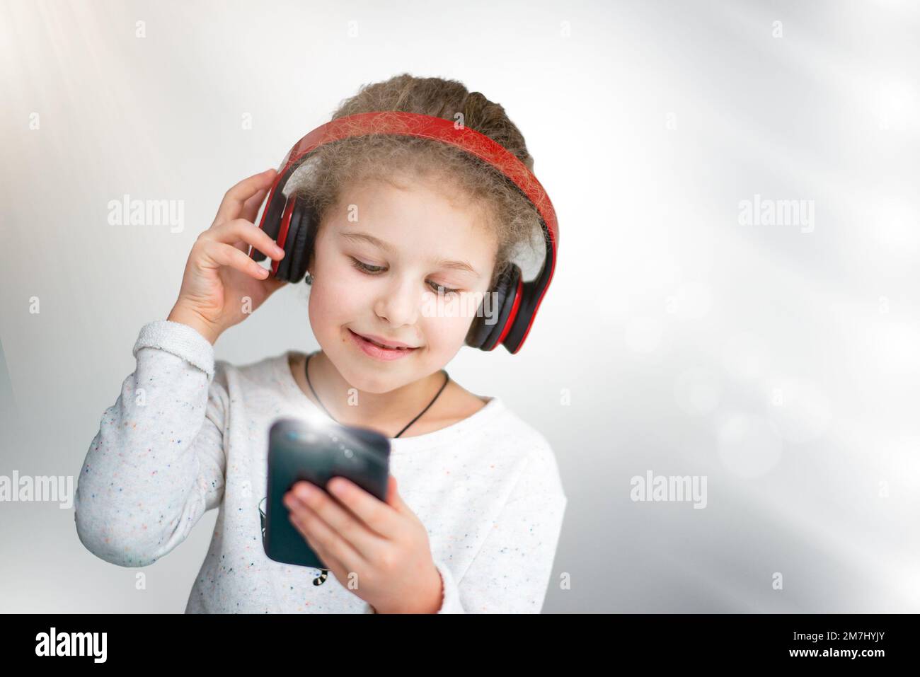 Una bella bambina ascolta la musica con le cuffie, tiene un telefono in mano. concetto di generazione Foto Stock