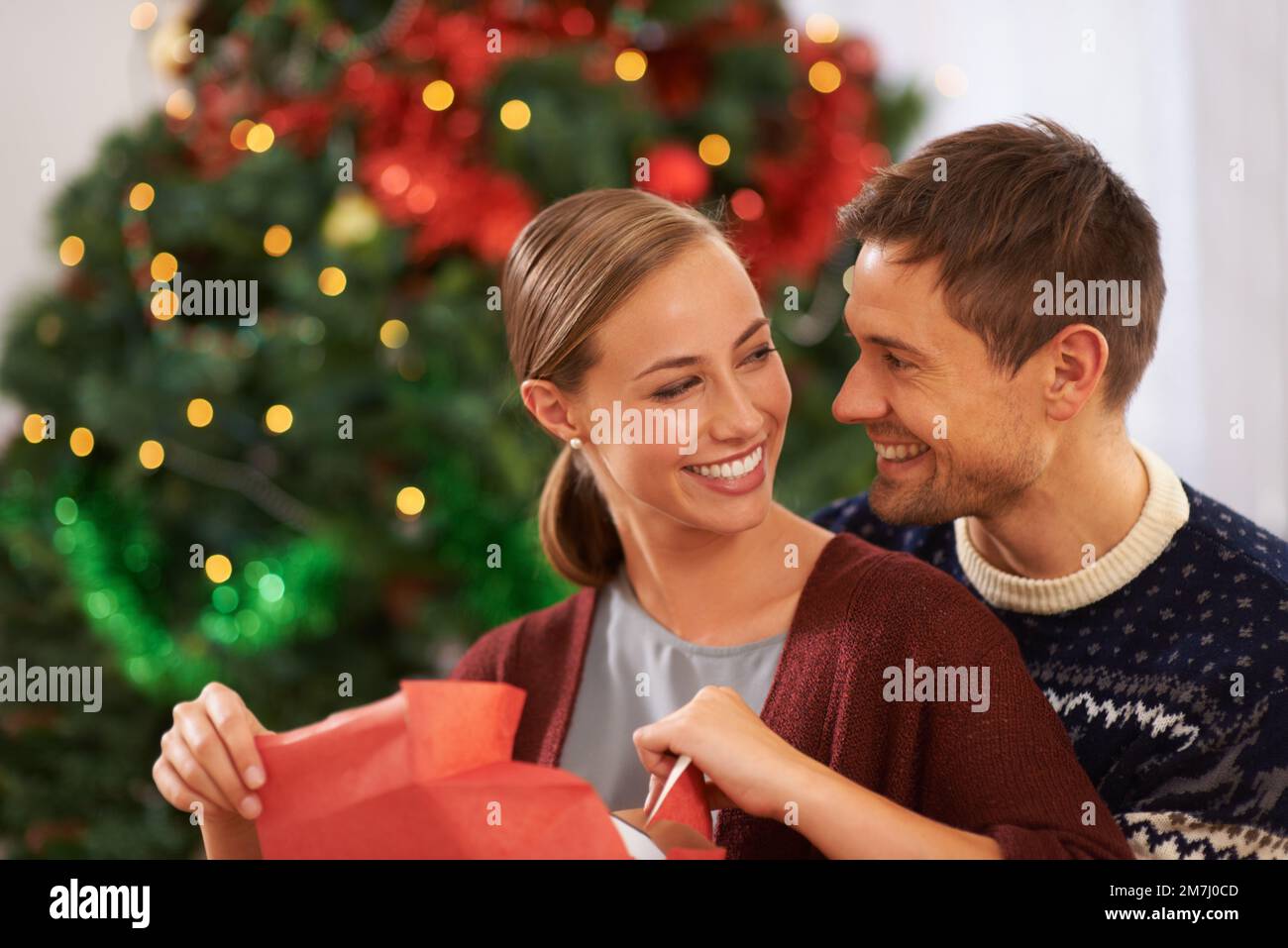 Non ha idea di cosa sia il suo dono. Una giovane coppia affettuosa il giorno di Natale. Foto Stock