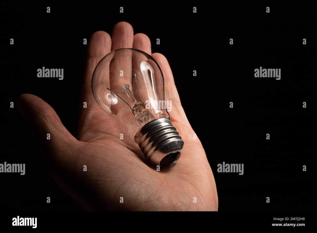 La mano di un uomo tiene una lampadina a incandescenza non funzionante su uno sfondo nero. Mancanza di idee e ispirazione, concetto di burnout Foto Stock