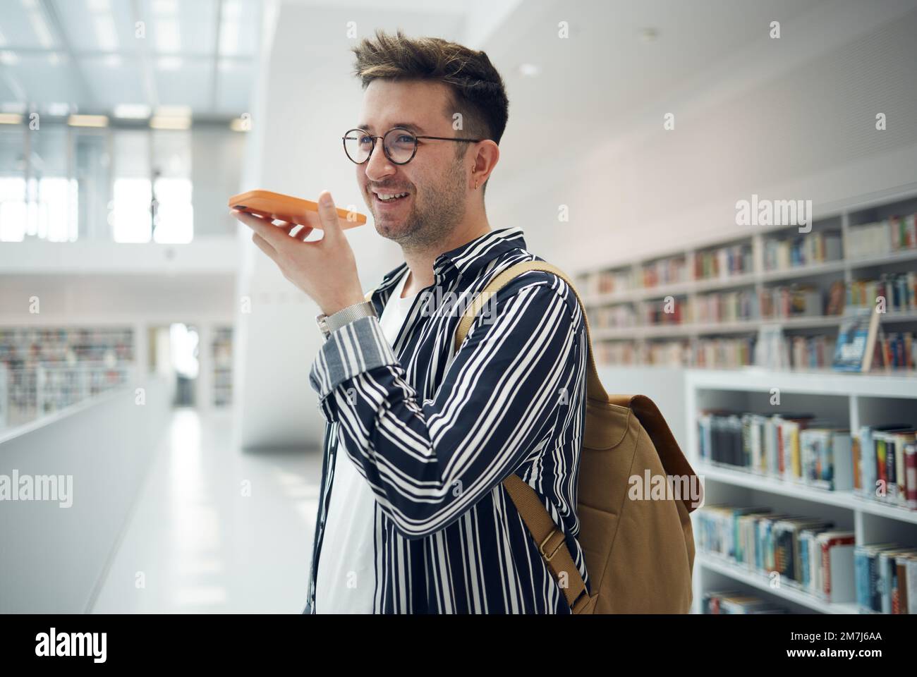 Uomo, telefonata e speaker in biblioteca, sorriso e connessione per la comunicazione, parlare e pianificazione data di studio. Giovane maschio, studente o accademico con Foto Stock