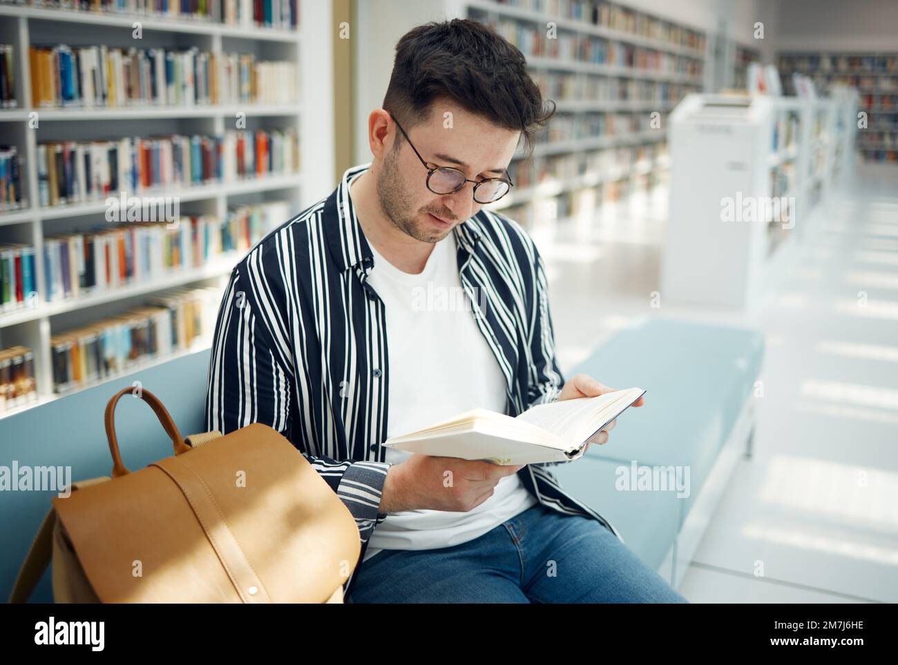 Educazione, lettura uomo e studente in biblioteca, conoscenza e studio per esami, test e intelligente. Giovane maschio, ragazzo e accademico con libro Foto Stock