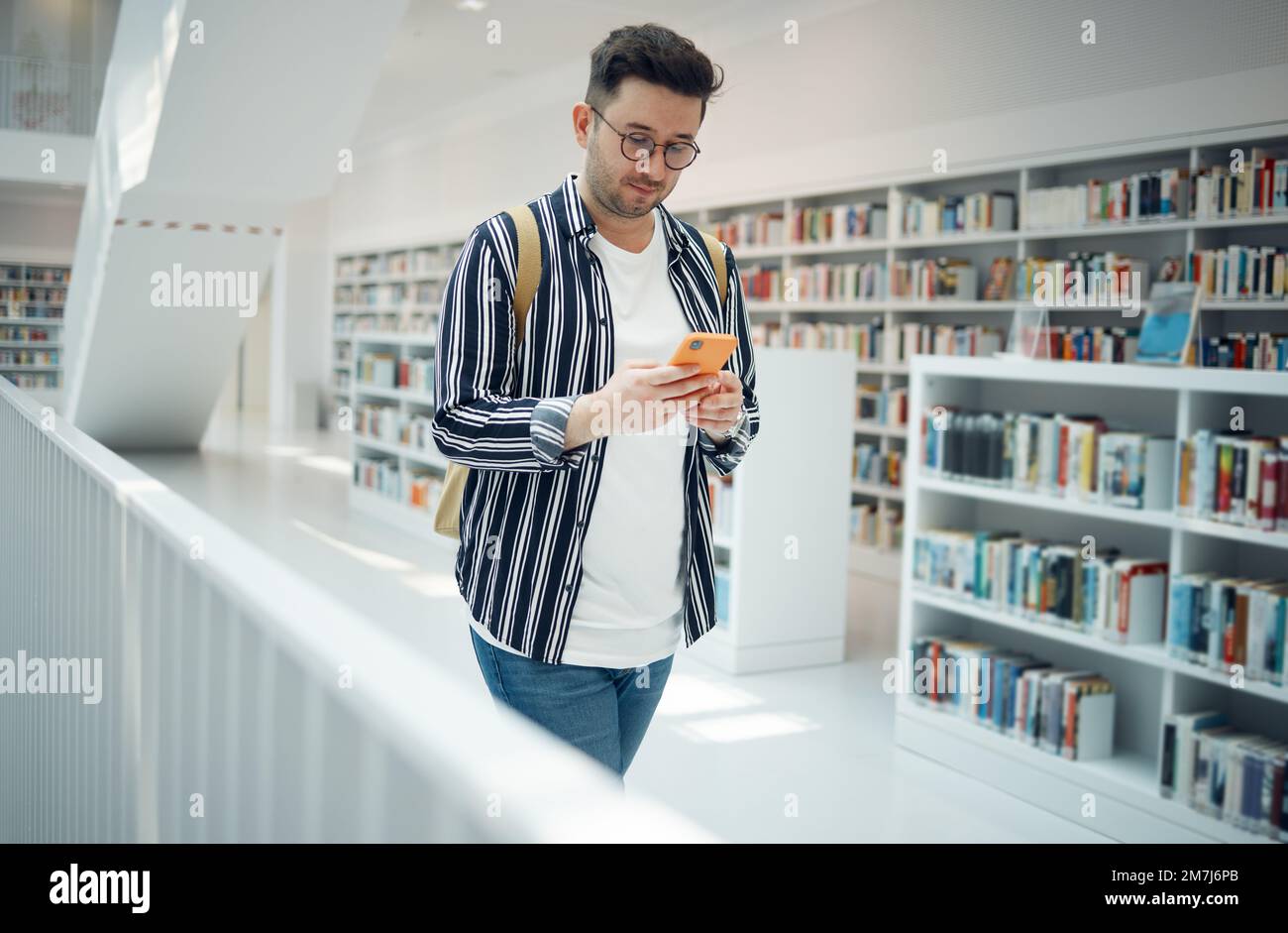 Istruzione, social media e uomo con un telefono in una biblioteca per la comunicazione, connessione wi-fi e chat online al college. Università, apprendimento e. Foto Stock