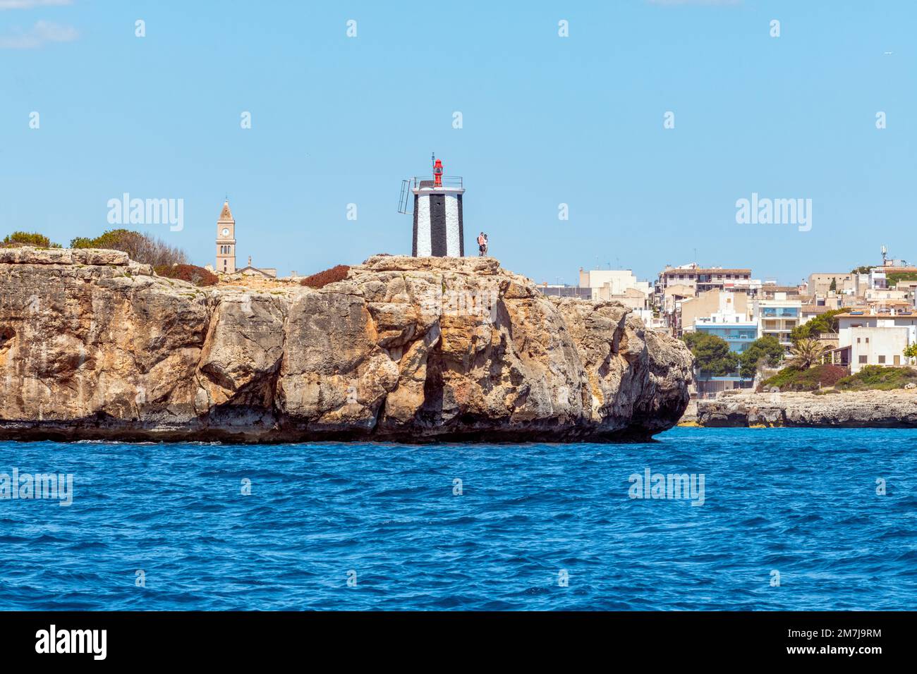 Due punti di riferimento di Porto Cristo sulla costa orientale di Maiorca. Il faro è costruito sulla roccia Morro de SA Carabassa e dietro di essa la chiesa del paese. Foto Stock