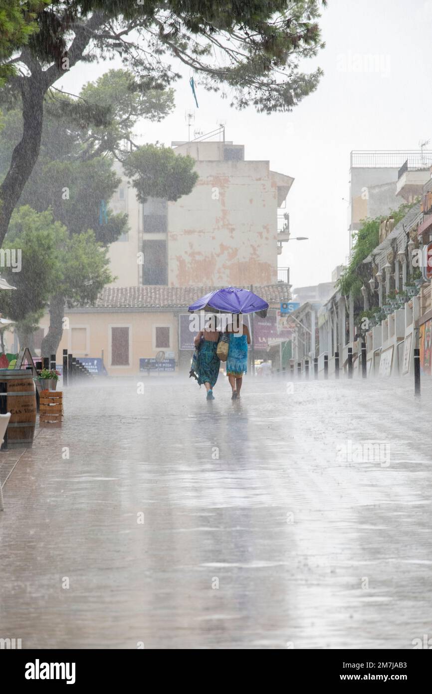 Due donne camminano attraverso la calda pioggia estiva sul lungomare di Porto Cristo. Foto Stock
