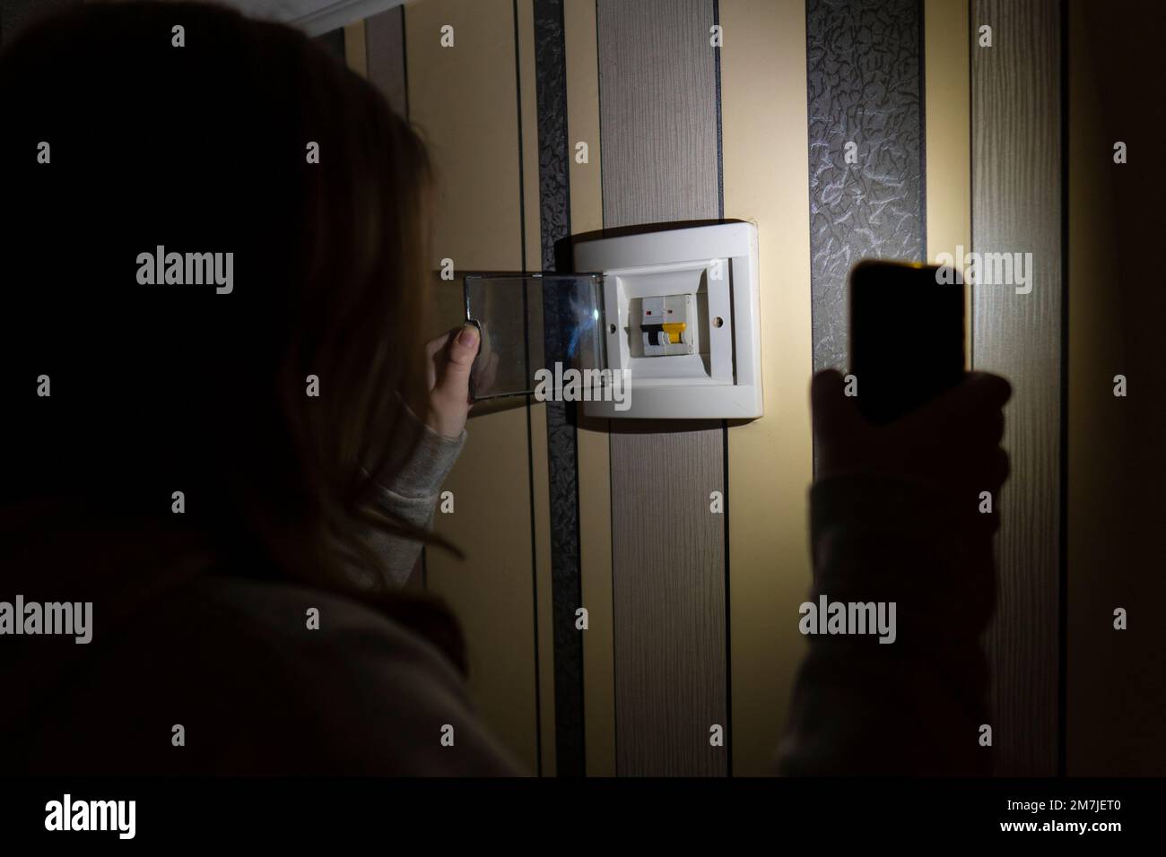 Ragazza con uno smartphone in mano controlla il quadro elettrico nella stanza. Blackout. Crisi energetica. Concetto di interruzione dell'alimentazione Foto Stock