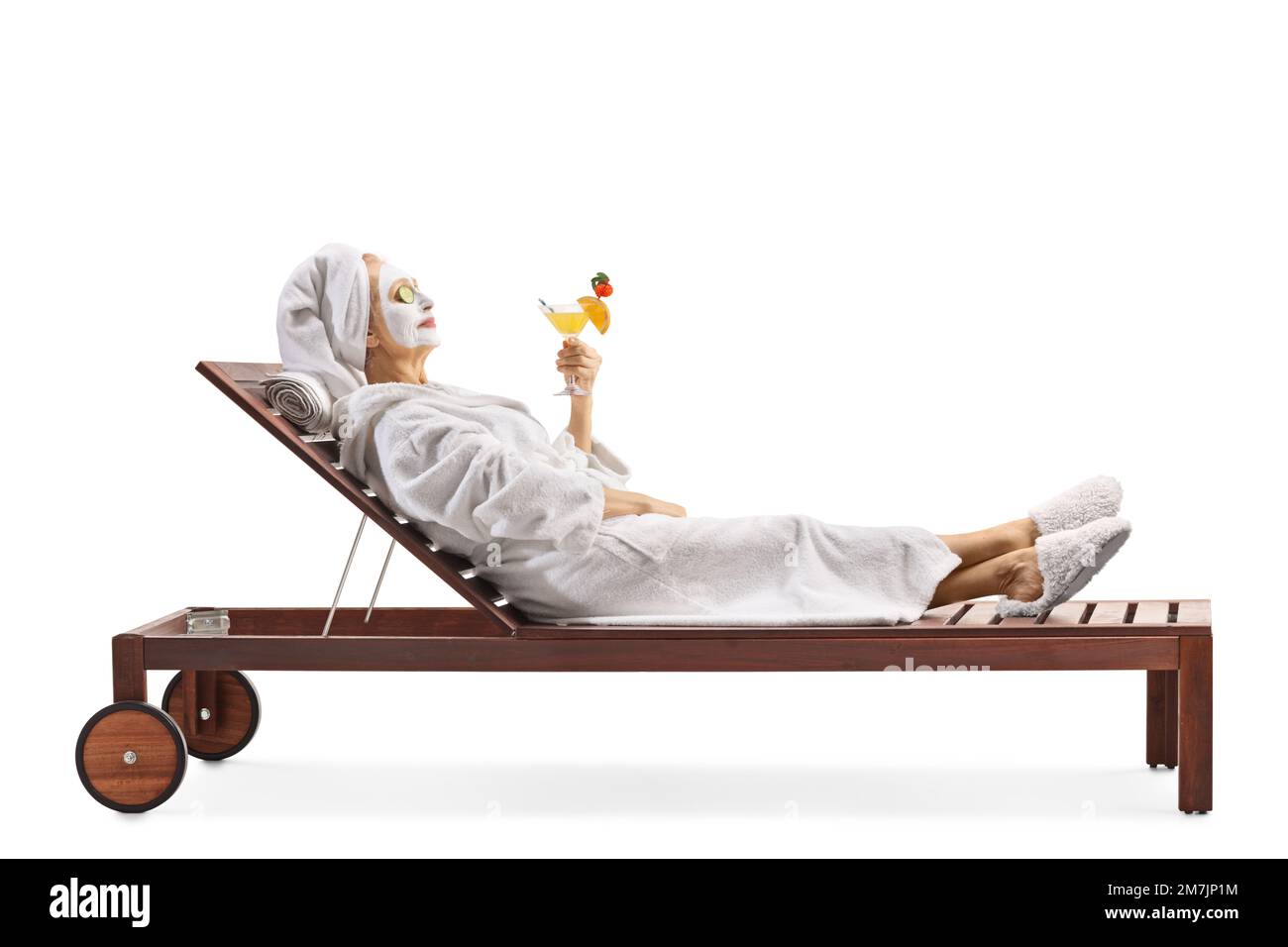 Donna in un accappatoio e capelli avvolti in asciugamano rilassante con una maschera per il viso e tenendo un cocktail isolato su sfondo bianco Foto Stock