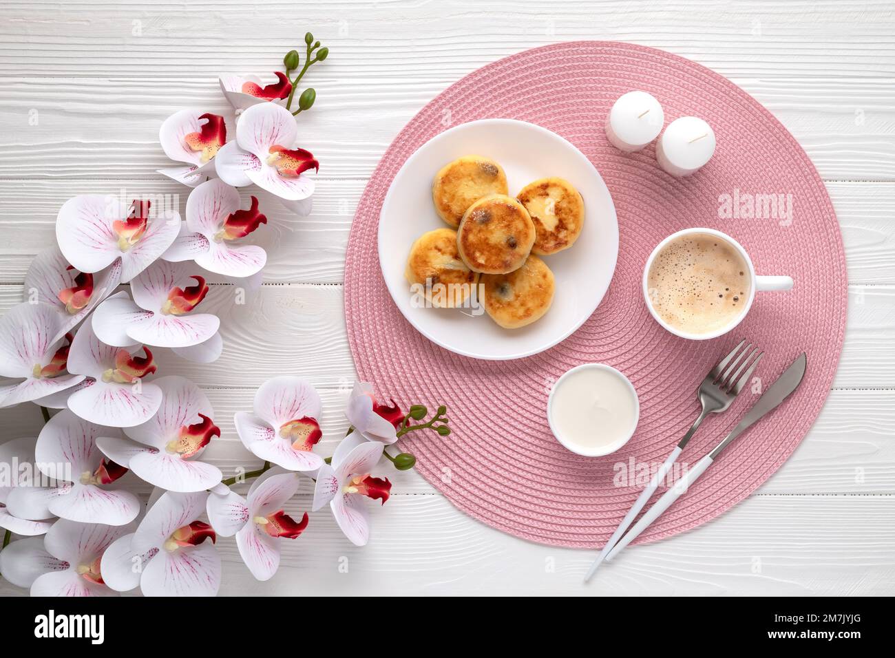 Frittelle di formaggio casolare con latte e fiori di orchidea su tavolo di legno bianco. Vista dall'alto. Biglietto di auguri per la festa della mamma. Cibo e bevande sfondo. Caffè, d Foto Stock