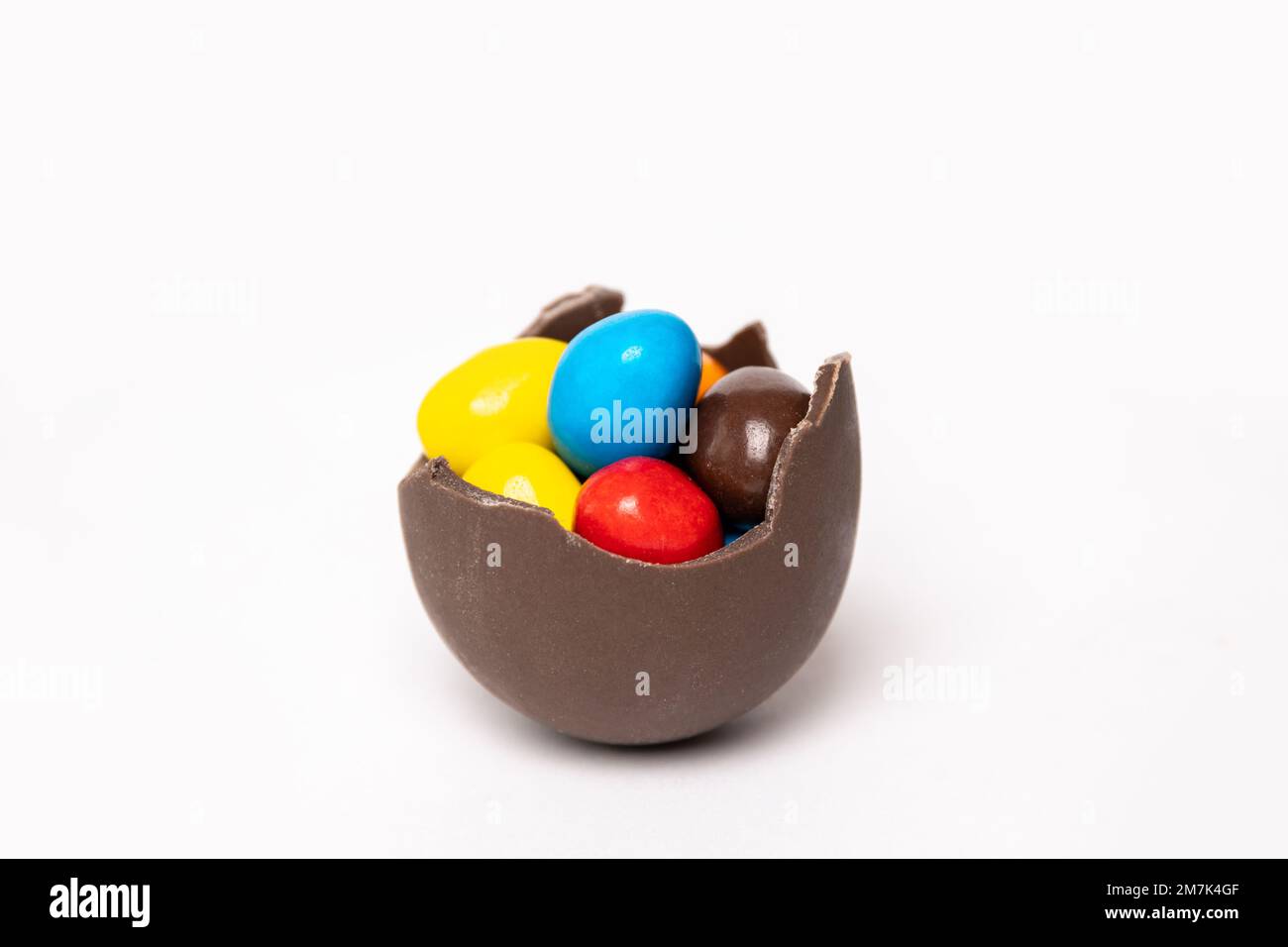 Uovo di pasqua al cioccolato cracked con piccole caramelle colorate rotonde su sfondo bianco, spazio copia, vista laterale. Cioccolatini per bambini. Concetto di Pasqua. Foto Stock