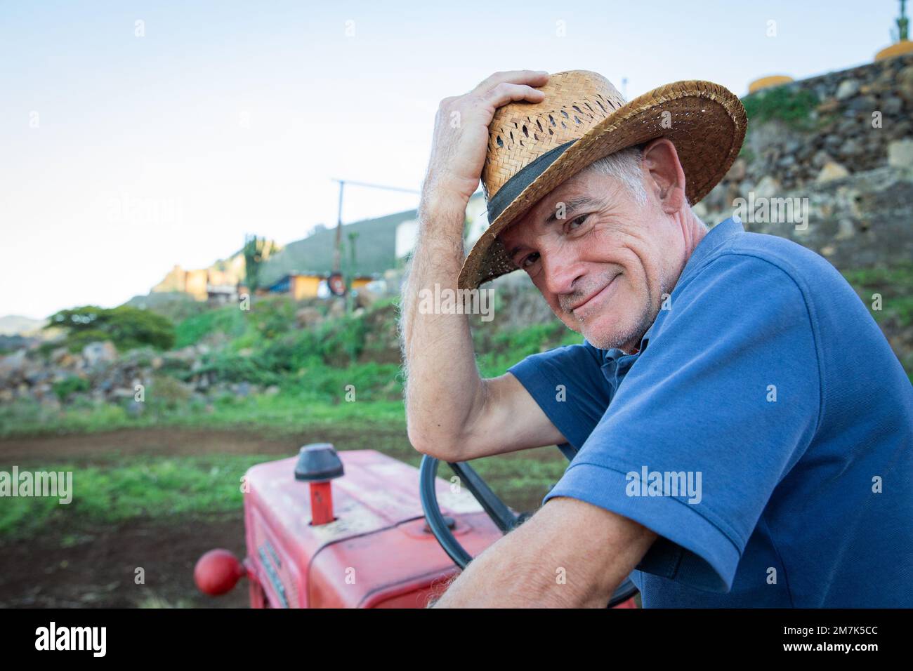 Un contadino sorridente tiene il cappello da cowboy mentre si siede sul trattore. Foto Stock