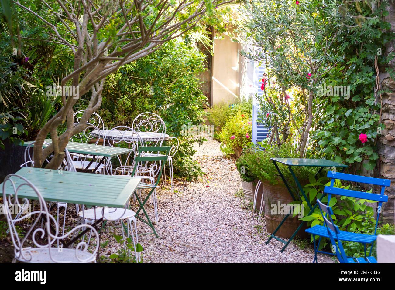 Intimo caffè con giardino con mobili in legno battuto nel mezzo del lussureggiante fogliame in Bretagna, Francia Foto Stock