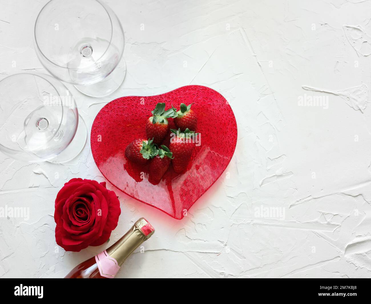 Data per San Valentino. Fragola su un piatto a forma di cuore con vino e bicchieri e una rosa Foto Stock