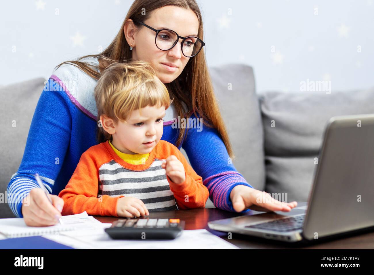 Giovane donna che lavora a casa con un notebook e un bambino in grembo Foto Stock