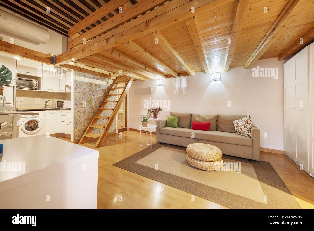 Appartamento loft con pannelli in legno di pino e mobili bianchi al piano terra, una scala in legno coordinata e pavimenti in parquet con tappeto beige e. Foto Stock