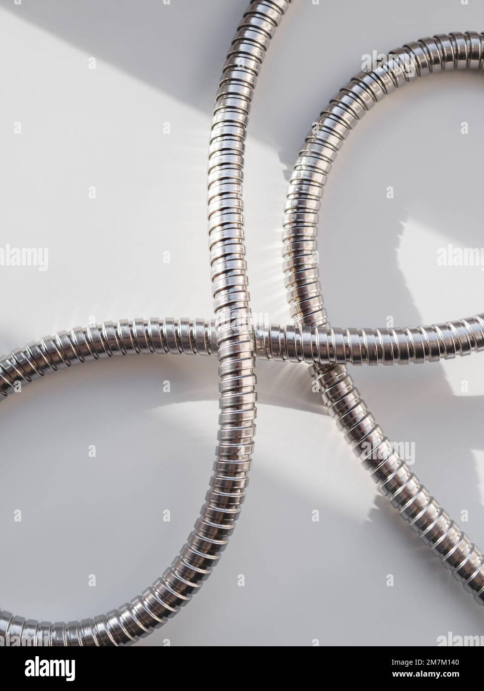 Tubo doccia in metallo su sfondo bianco. Tubo cromato flessibile. Tubo corrugato su striscione geometrico con spazio copia su luce solare dura Foto Stock