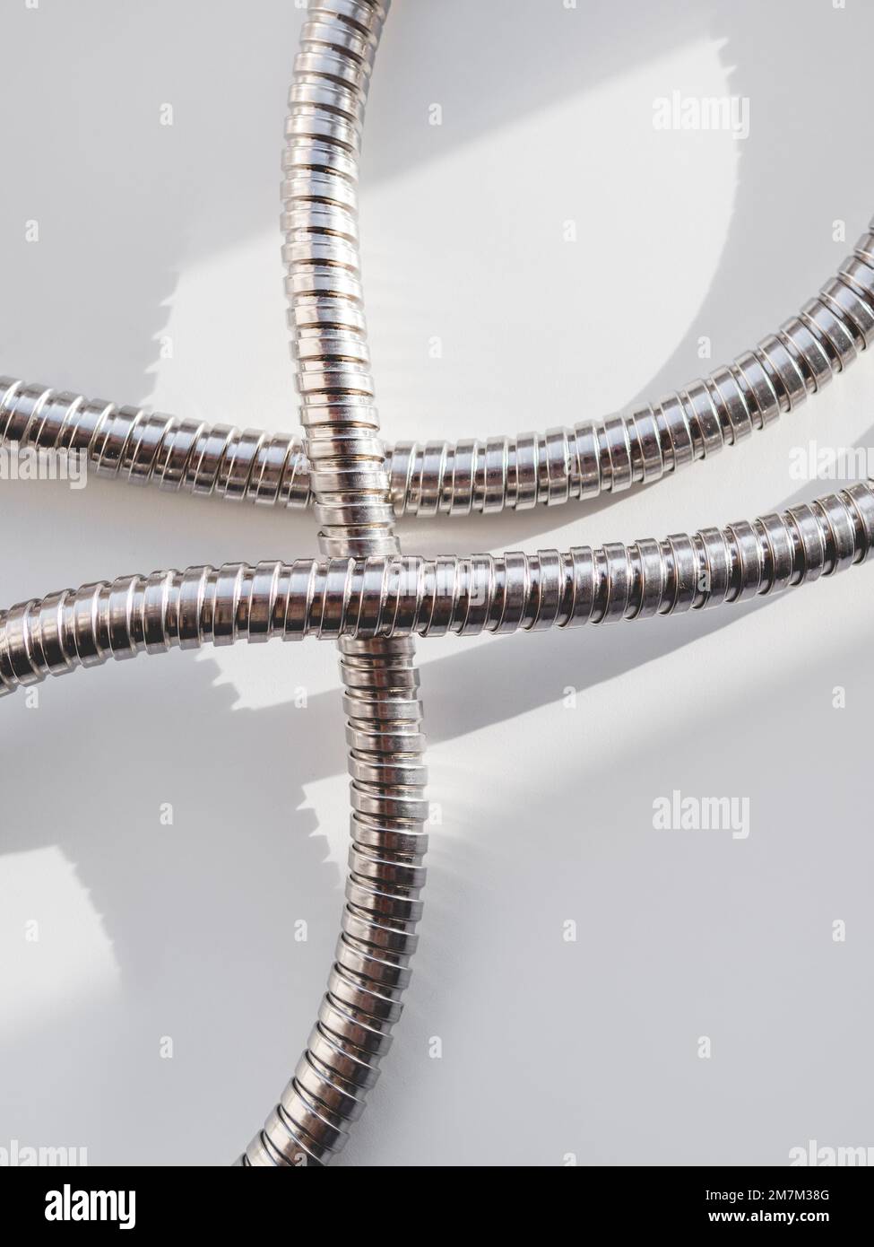 Tubo doccia in metallo su sfondo bianco. Tubo cromato flessibile. Tubo corrugato su striscione geometrico con spazio copia su luce solare dura Foto Stock