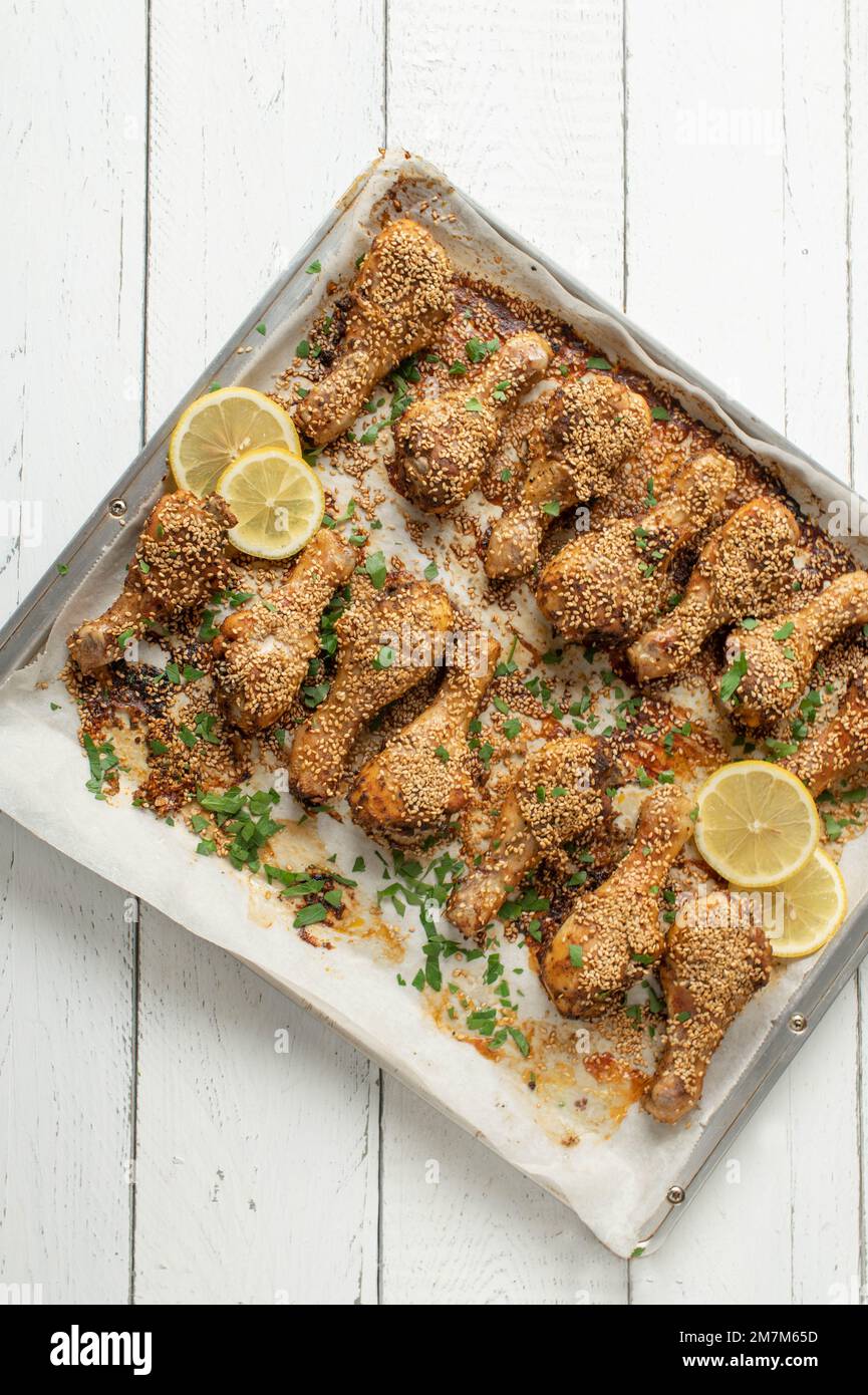 Pollo al sesamo marinato con pasta harissa su una teglia da forno isolata su sfondo di legno bianco con spazio per il testo Foto Stock