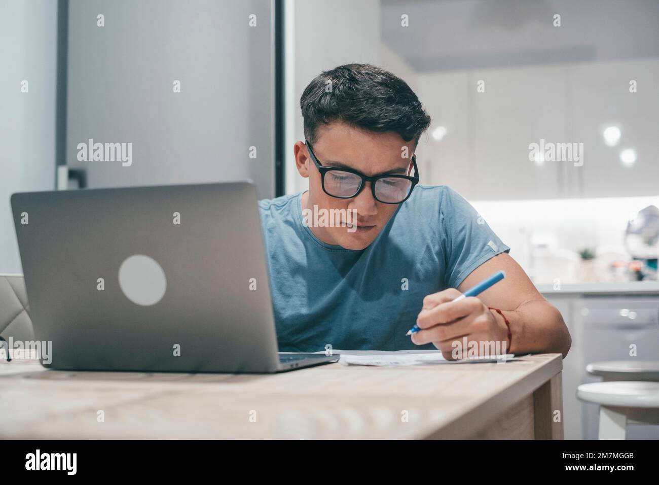 Un giovane adolescente che studia e lavora a casa di notte sul tavolo utilizzando un PC portatile sorridendo e divertendosi a fare i compiti. Foto Stock