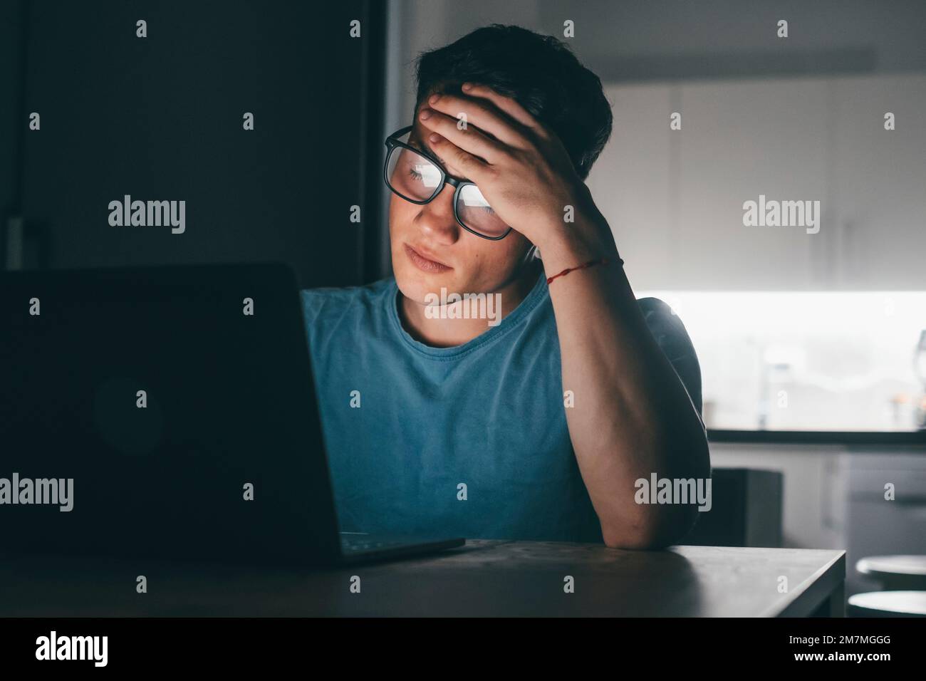 Un giovane malato e stanco che si sente male toccando gli occhi e il viso di notte dopo il lavoro. Adolescente maschio con mal di testa di lavoro. Foto Stock