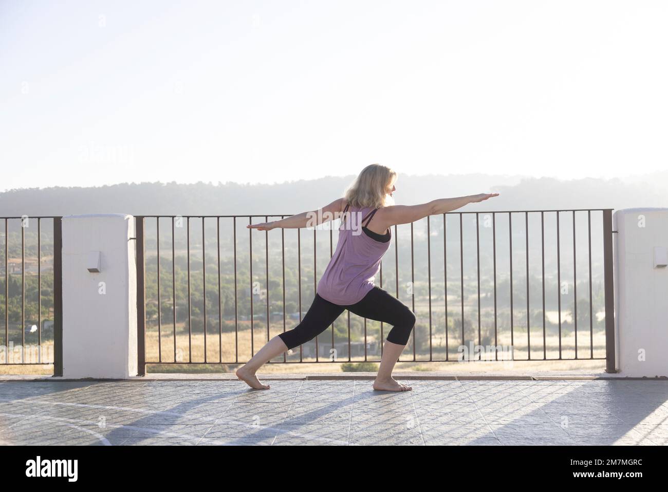 Donna bionda che pratica yoga all'alba su una terrazza in Spagna Foto Stock
