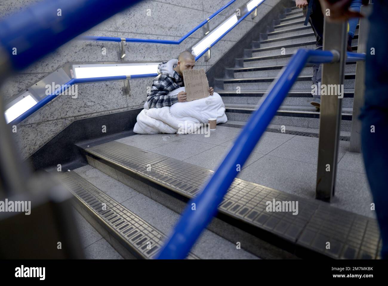 Londra, Inghilterra, Regno Unito. L'uomo senza casa che implora sui gradini di Victoria Underground Stration con un segno 'senza casa si prega di aiutare £1 verso un ostello Foto Stock