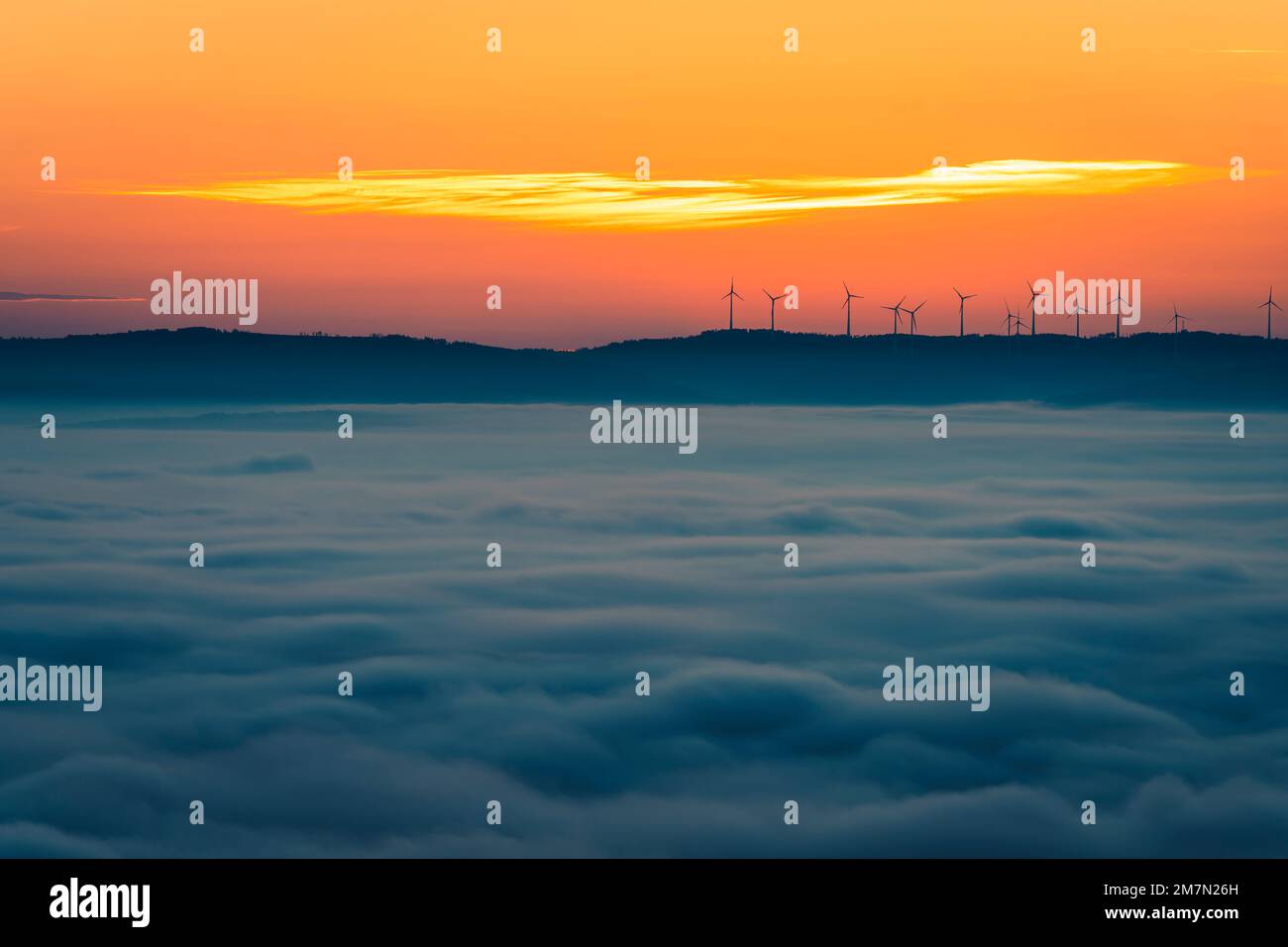 Turbine eoliche silentate all'orizzonte vicino a Kassel, mattina rosso nel cielo, inversione del tempo sopra la città Foto Stock