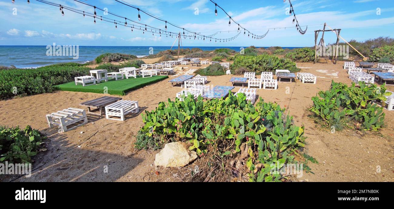 Tavoli e sgabelli primitivi di un bar sulla spiaggia a Punta Braccetto, Sicilia Foto Stock