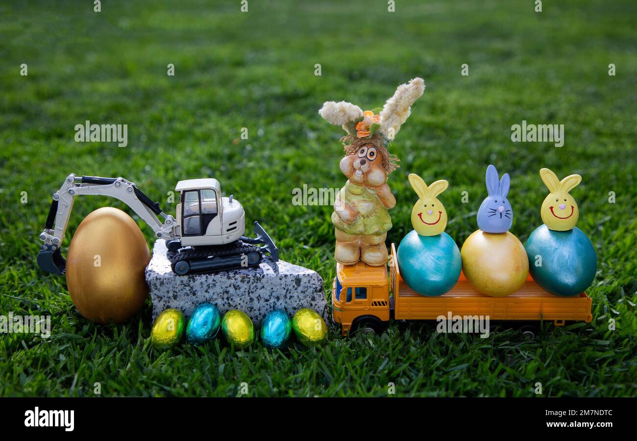 Biglietto d'auguri per le imprese di costruzione in vacanza di Pasqua. Composizione di un modello di escavatore, dumper, verniciato e. Foto Stock