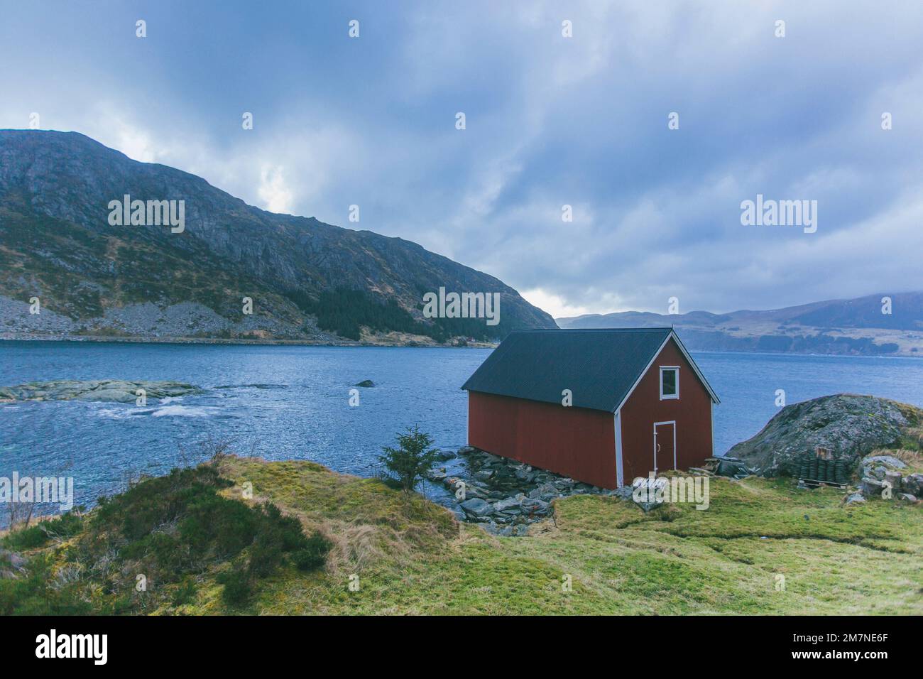 Solitario capanna di pesca rossa sul fiordo in Norvegia, tipico paesaggio fiordo con piccole isole, isolamento dal mondo esterno, casa sul mare, rifugio iconico Foto Stock