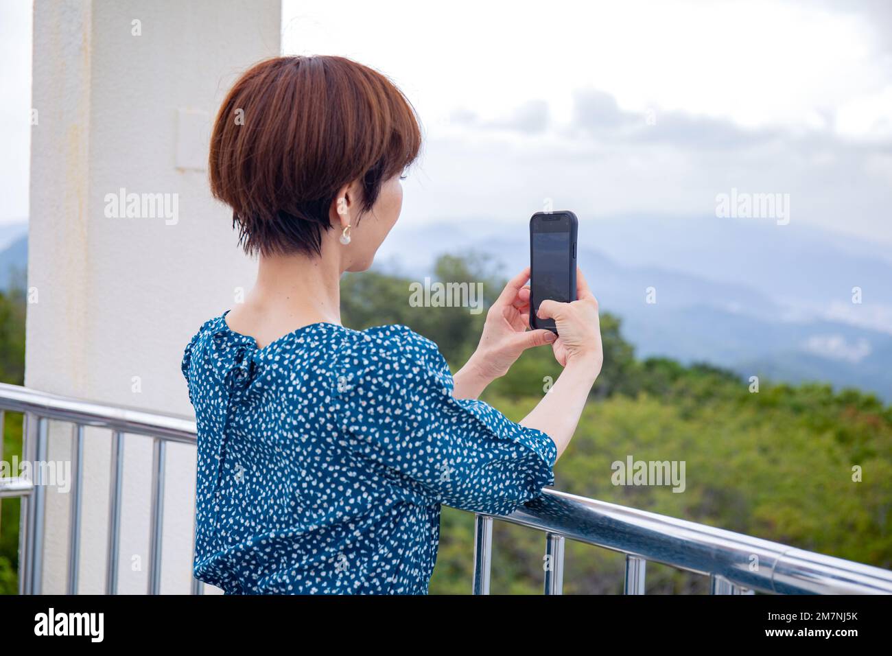Una donna giapponese matura che scattava una foto con il suo cellulare, su una piattaforma panoramica sopra la città. Foto Stock