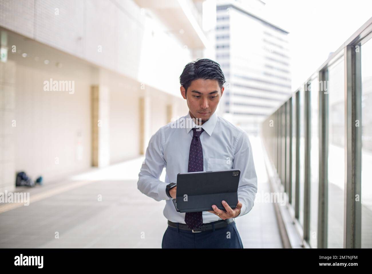 Un giovane uomo d'affari in città, in movimento, in piedi su una passerella utilizzando il suo computer portatile. Foto Stock